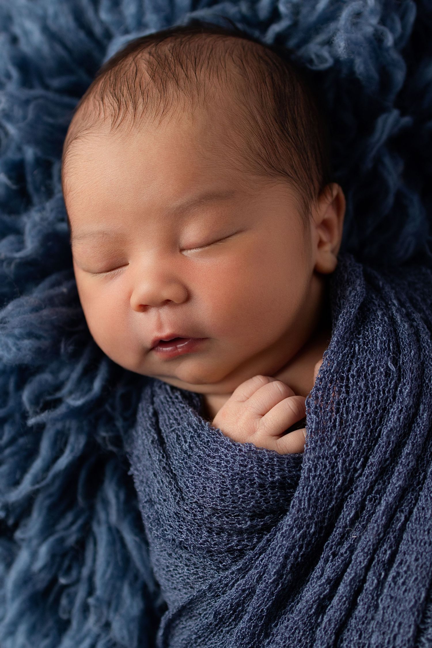 Peaceful sleeping newborn baby wrapped in a blue swaddle on a soft blue fluffy blanket.