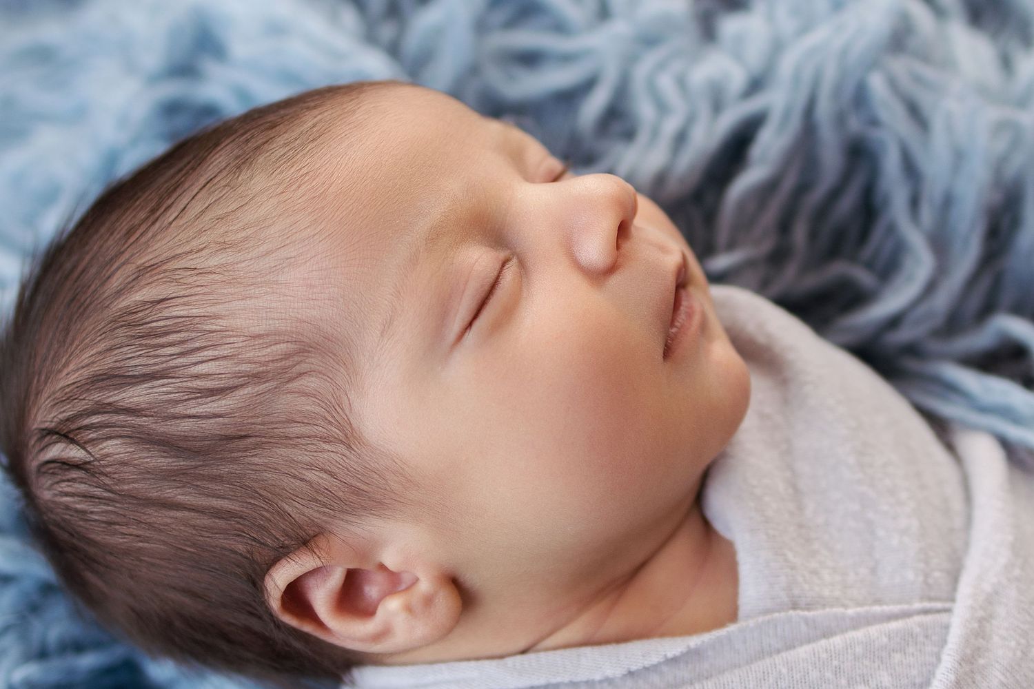 Peaceful newborn baby sleeping on a soft blue blanket, wrapped in a gray swaddle.