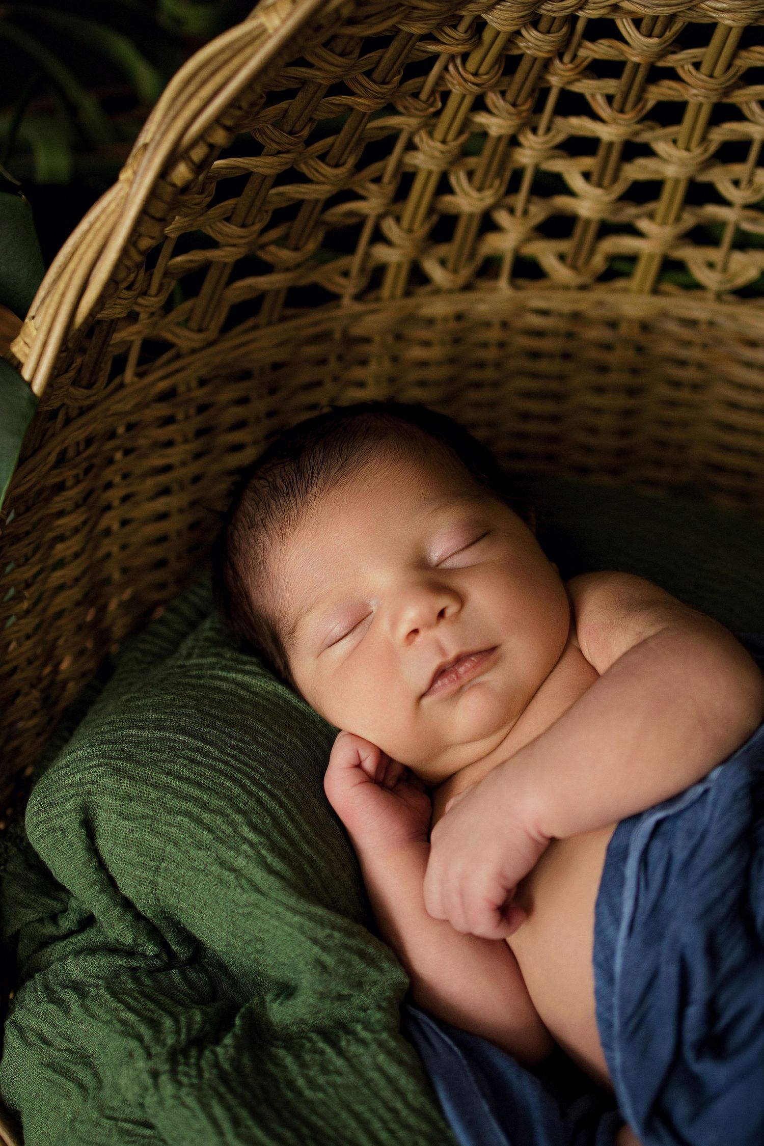 Peaceful newborn baby sleeping in a wicker basket with green and blue blankets.