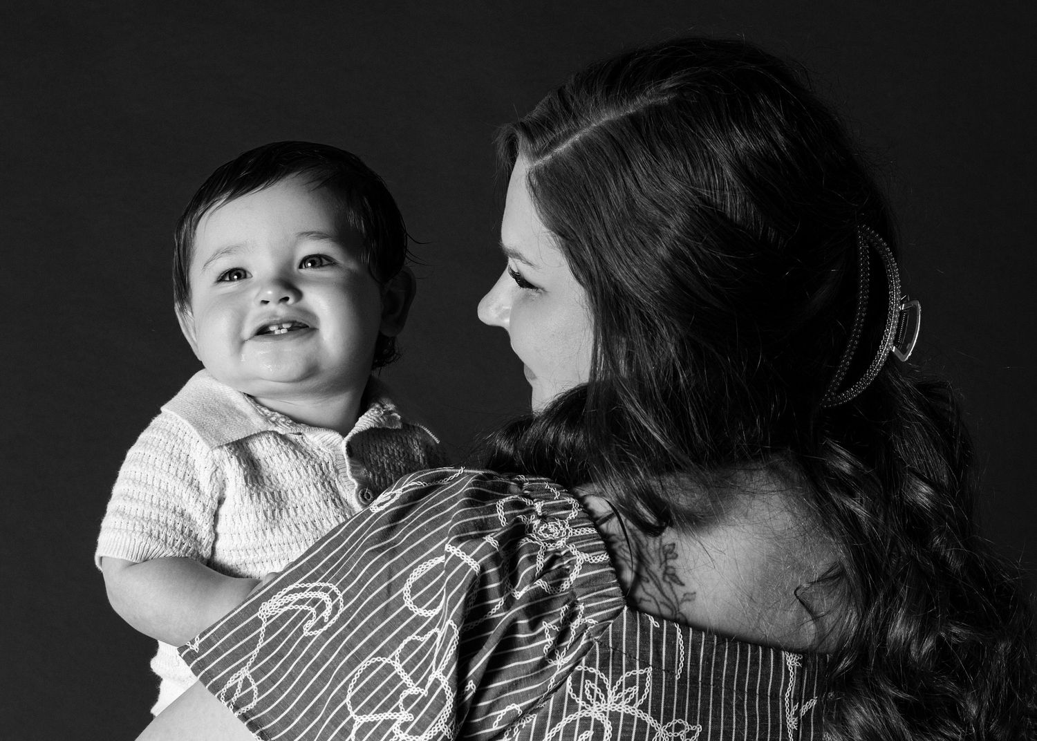 Black and white portrait of a smiling baby held by a woman with long hair in a studio setting.