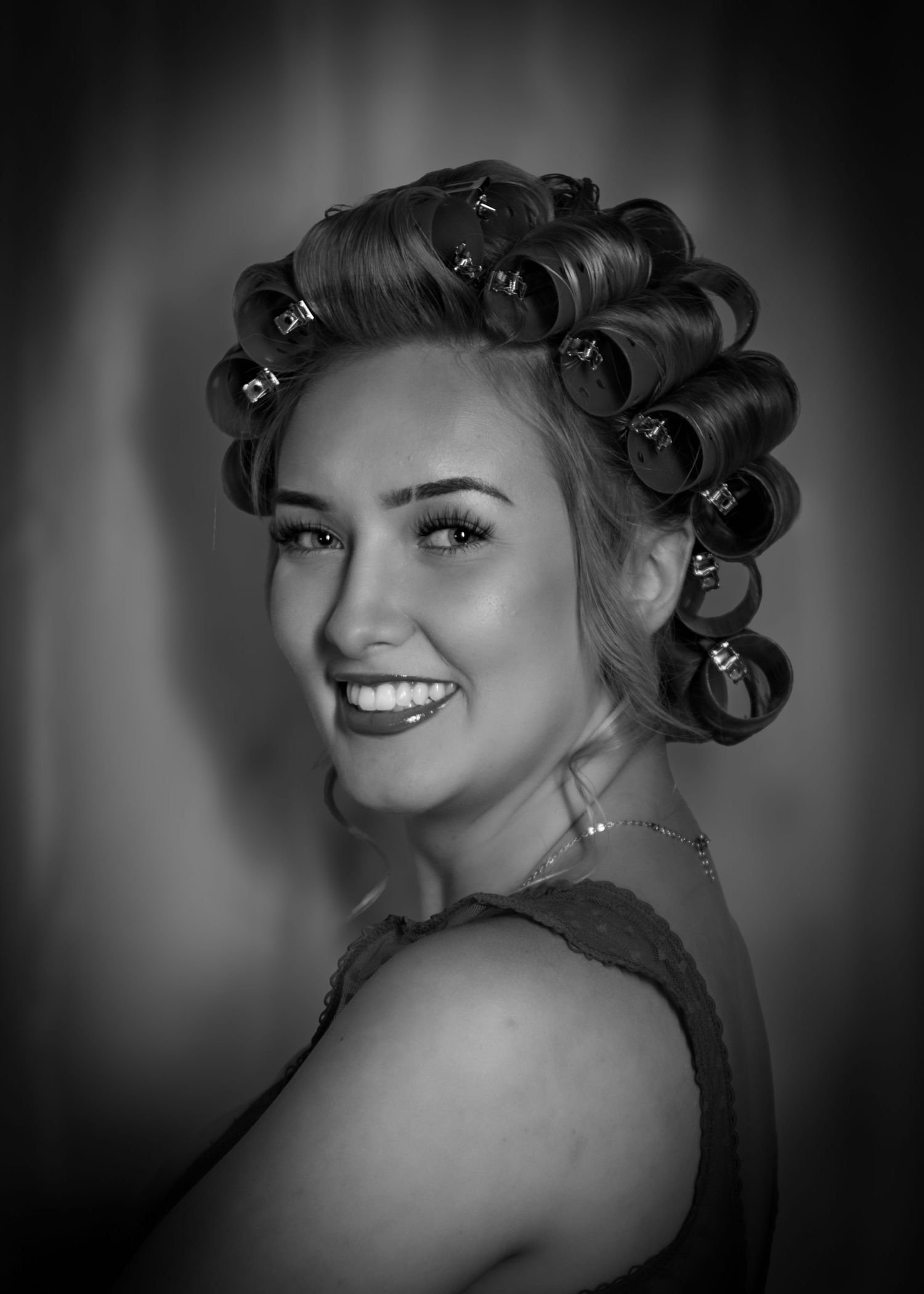 Smiling woman with large hair rollers poses in black and white portrait photo.