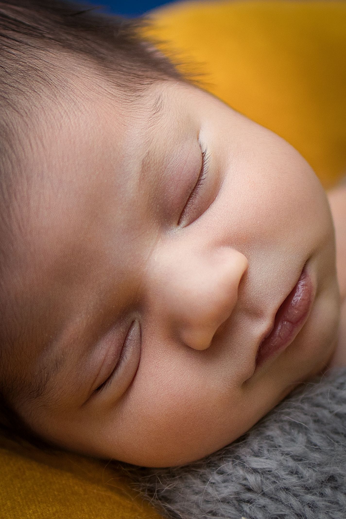 Close-up of a peaceful newborn baby sleeping on a soft gray and yellow blanket.