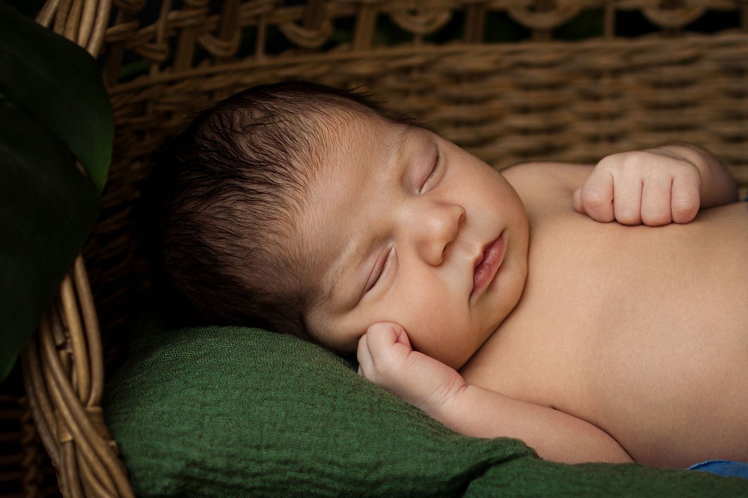 Peaceful newborn baby sleeping on a green blanket in a wicker basket, perfect newborn photography portrait.