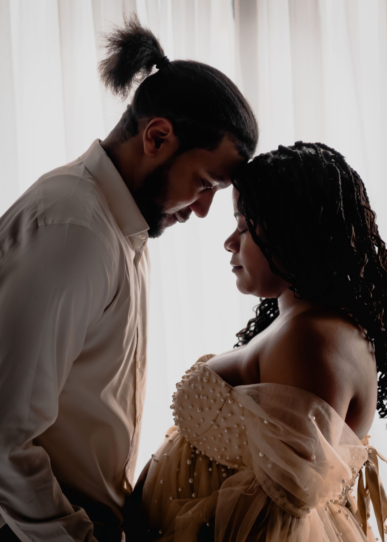 Artistic silhouette of couple in formal wear sharing an intimate moment against white backdrop.