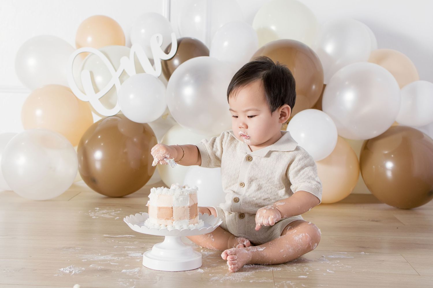 Baby's first birthday cake smash photo with neutral beige and white balloon backdrop and \