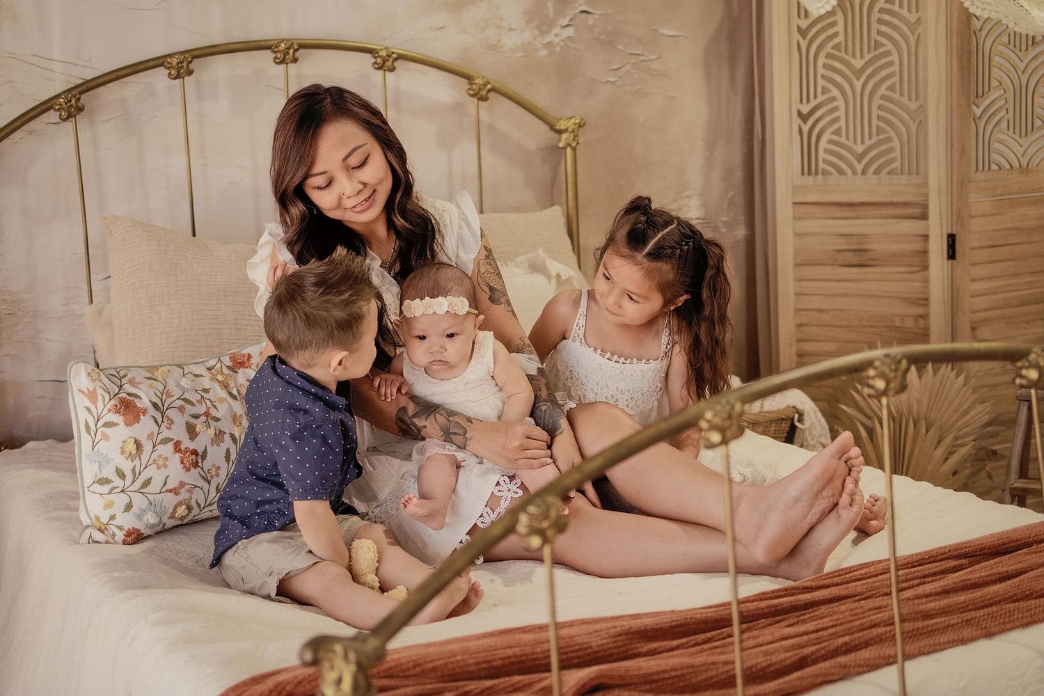 A mother sits on a vintage brass bed with her three young children, sharing a warm and tender family moment.