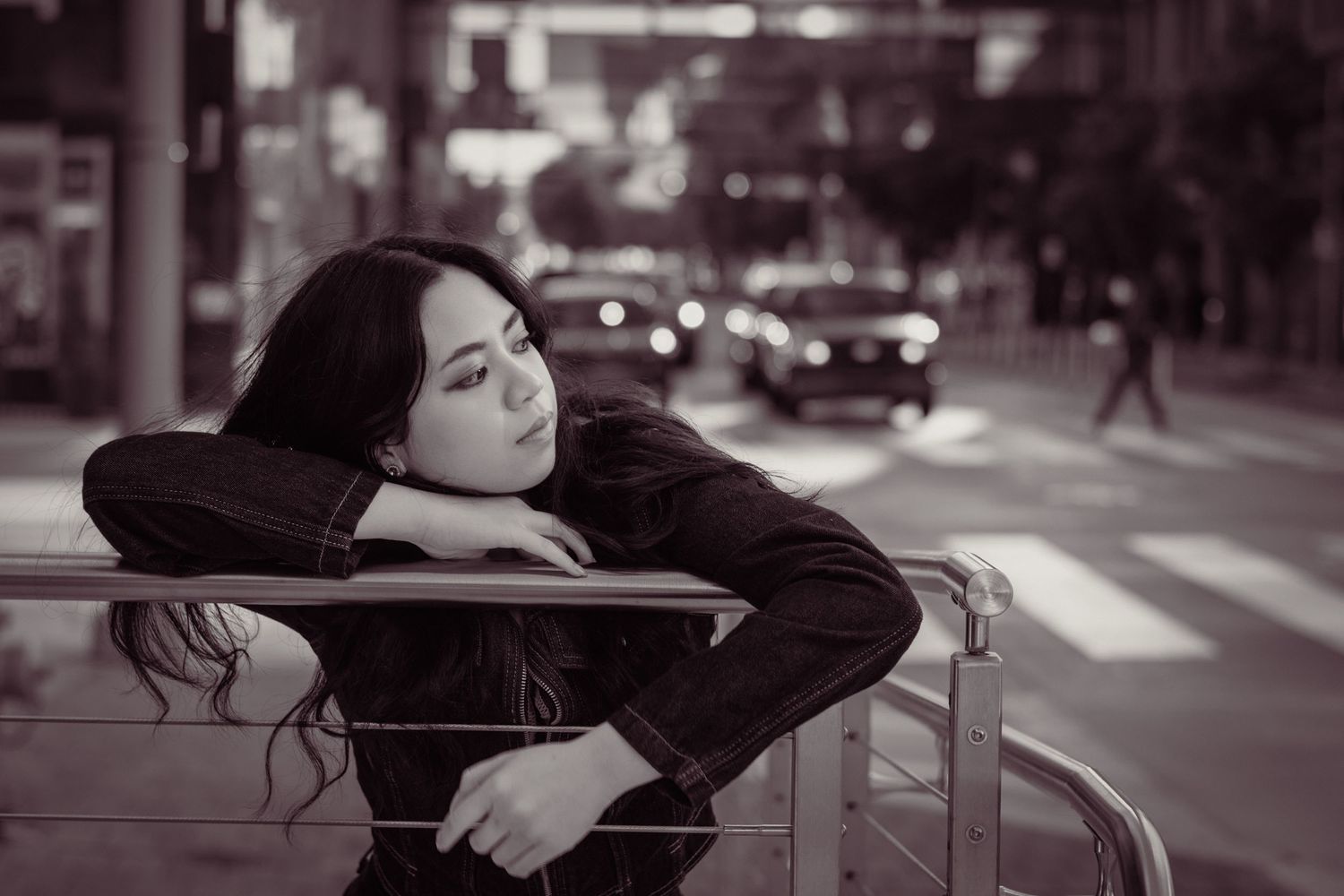 Black and white photo of a young woman resting her head on a metal railing on a city street.