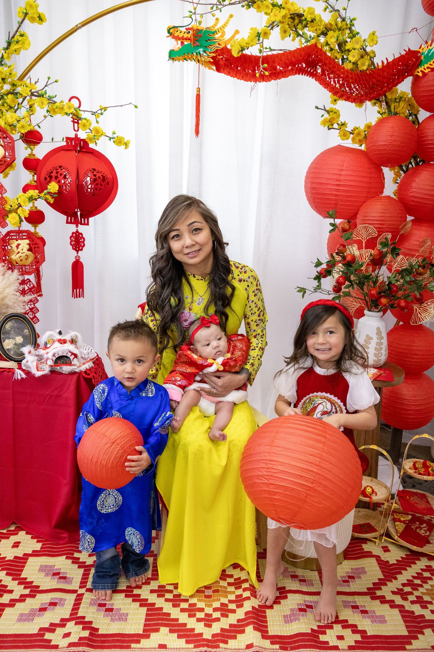 Family in traditional Vietnamese ao dai attire celebrating Lunar New Year with red lanterns and festive decorations.