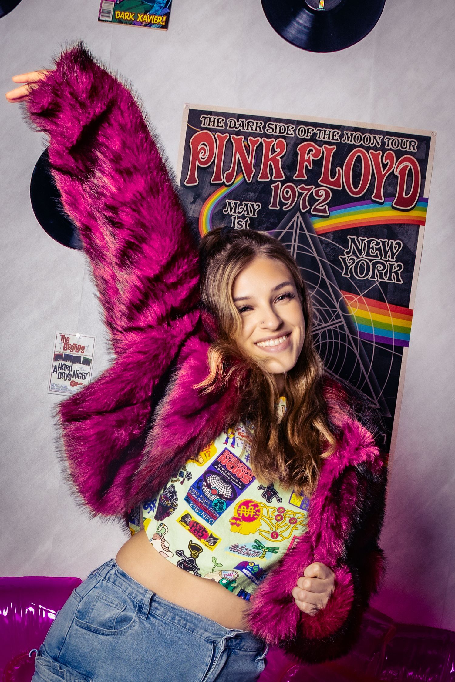 Young woman in pink fur coat poses in front of Pink Floyd 1972 Dark Side of the Moon Tour poster with vinyl records.