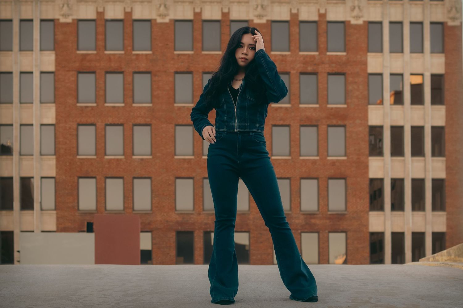 Woman in dark denim flare jumpsuit posing outdoors in front of brick building.