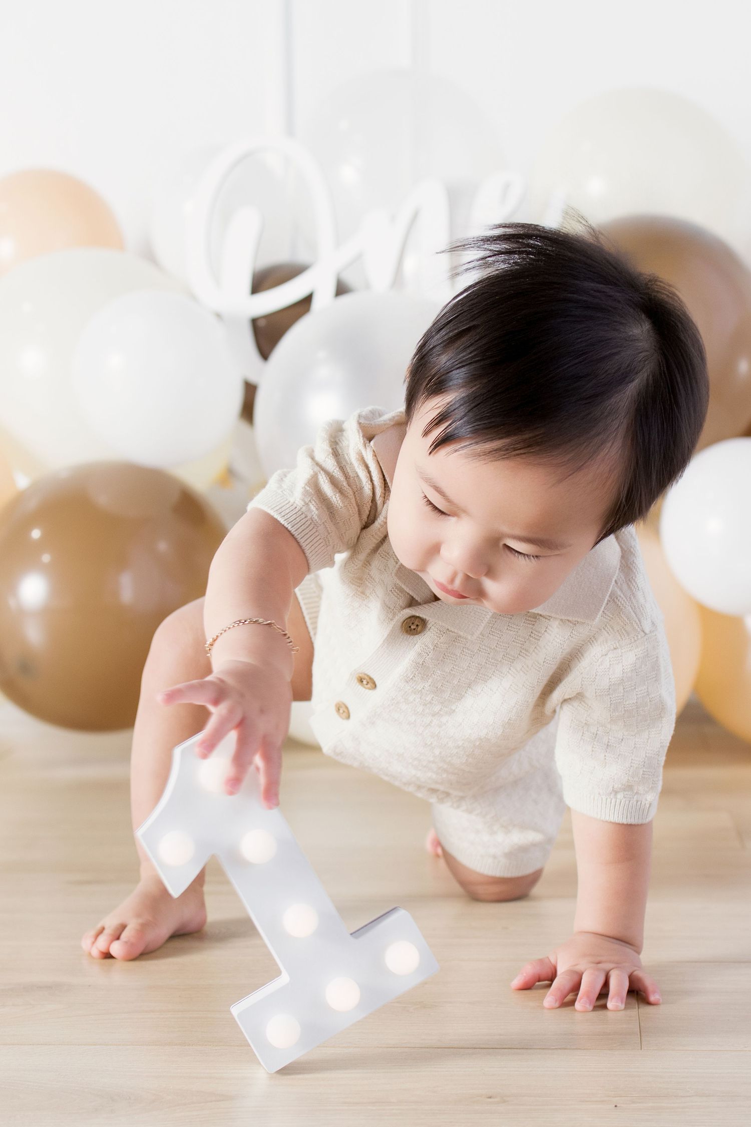 Baby's first birthday photoshoot with number one light-up sign, balloons, and 'One' script decoration.