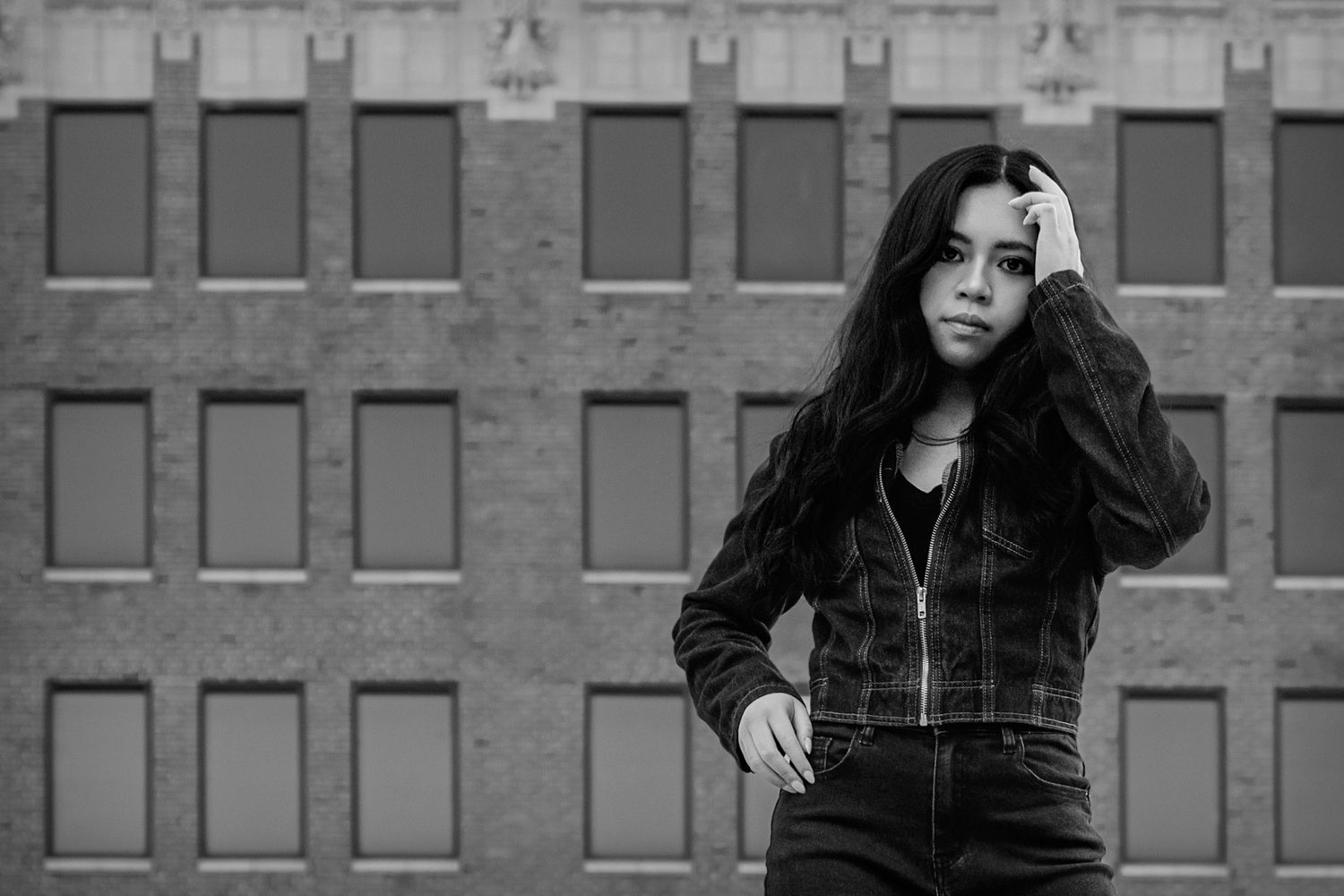 Black and white portrait of a young woman posing outdoors in front of a brick building.