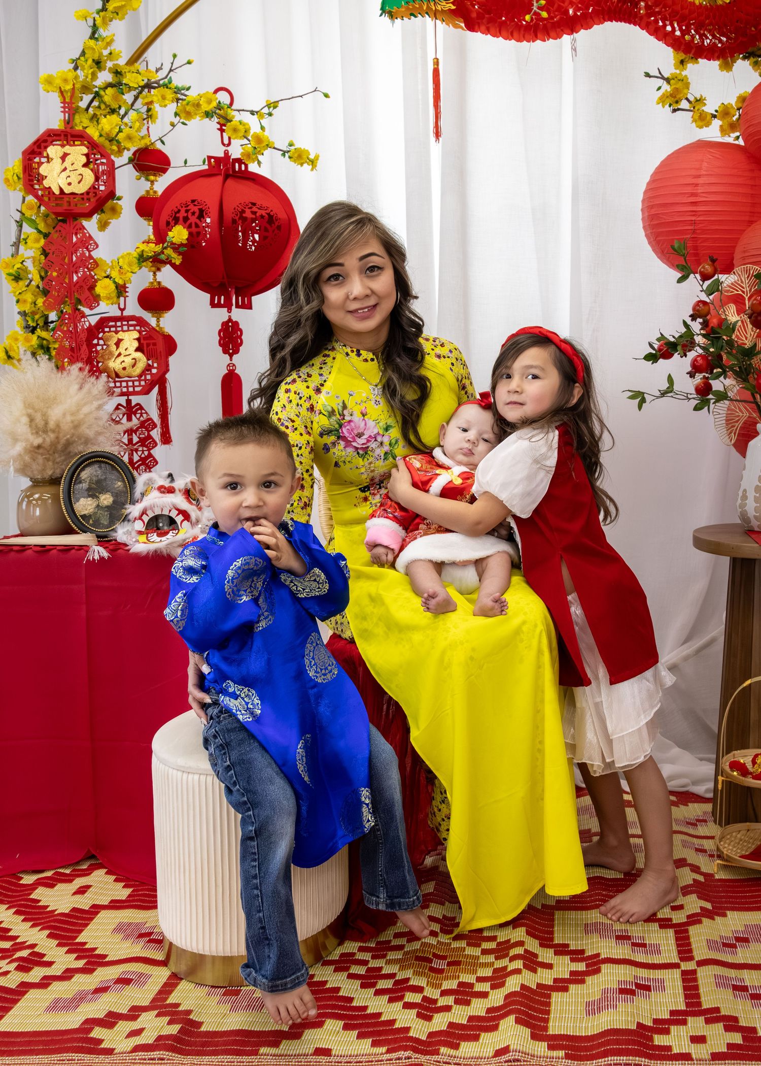 Family in traditional Vietnamese ao dai poses for Lunar New Year photo with red lanterns and yellow blossoms.