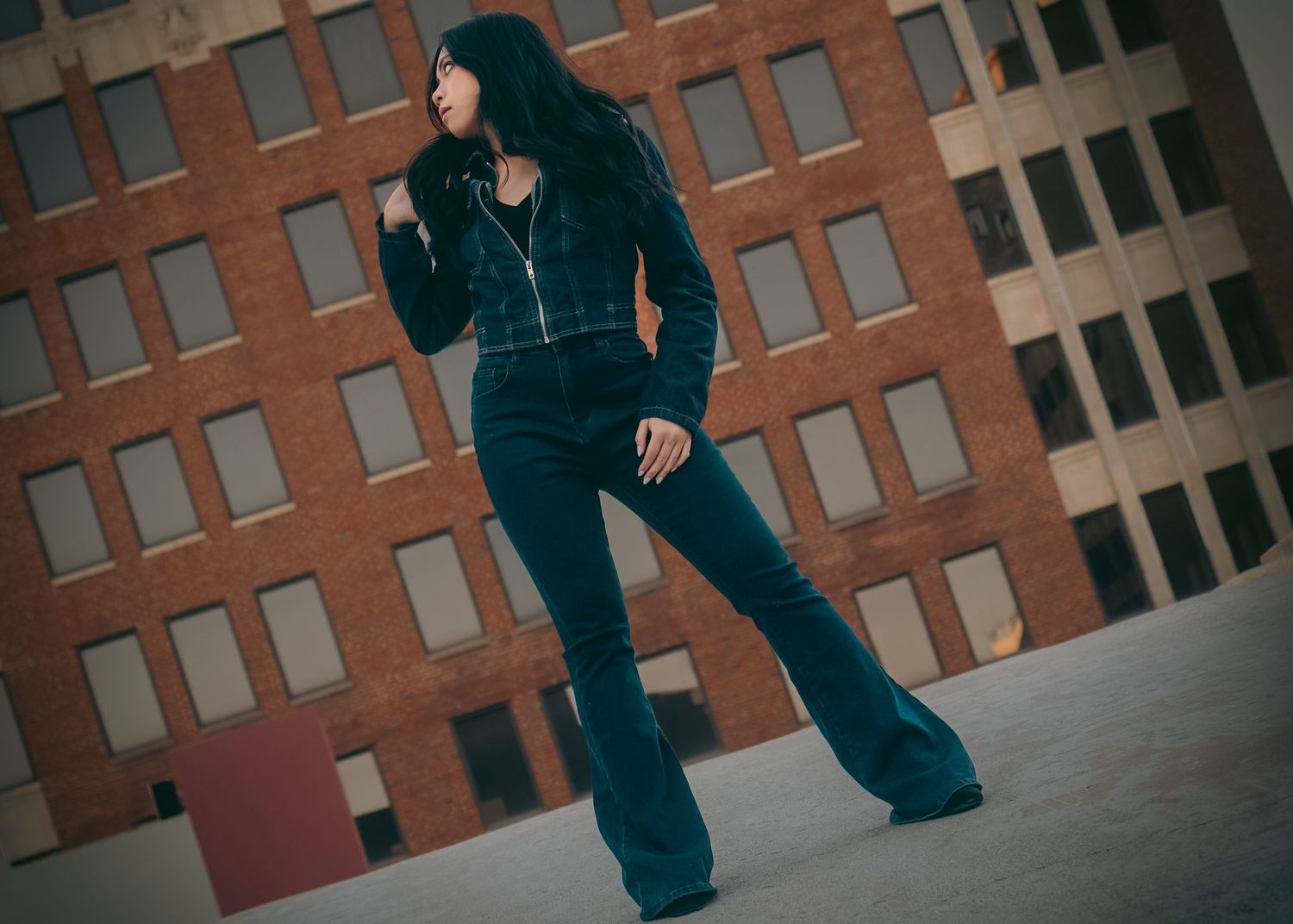 Woman in all-black outfit with flare pants poses outdoors against a brick building backdrop.