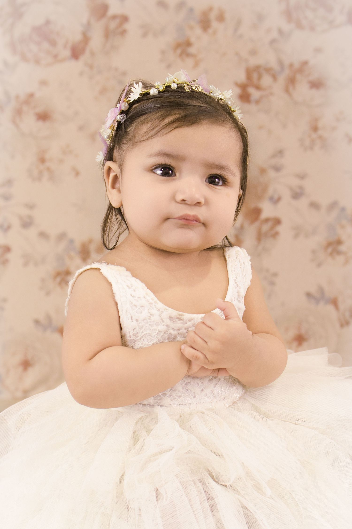 Adorable baby girl in white lace tutu dress wearing delicate floral crown headband.