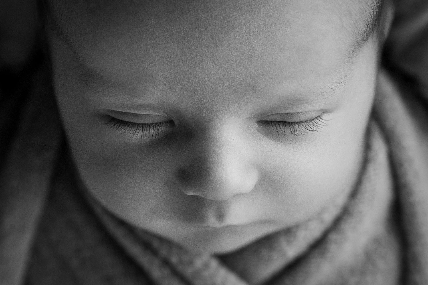 Black and white close-up portrait of a sleeping newborn baby wrapped in a soft blanket.