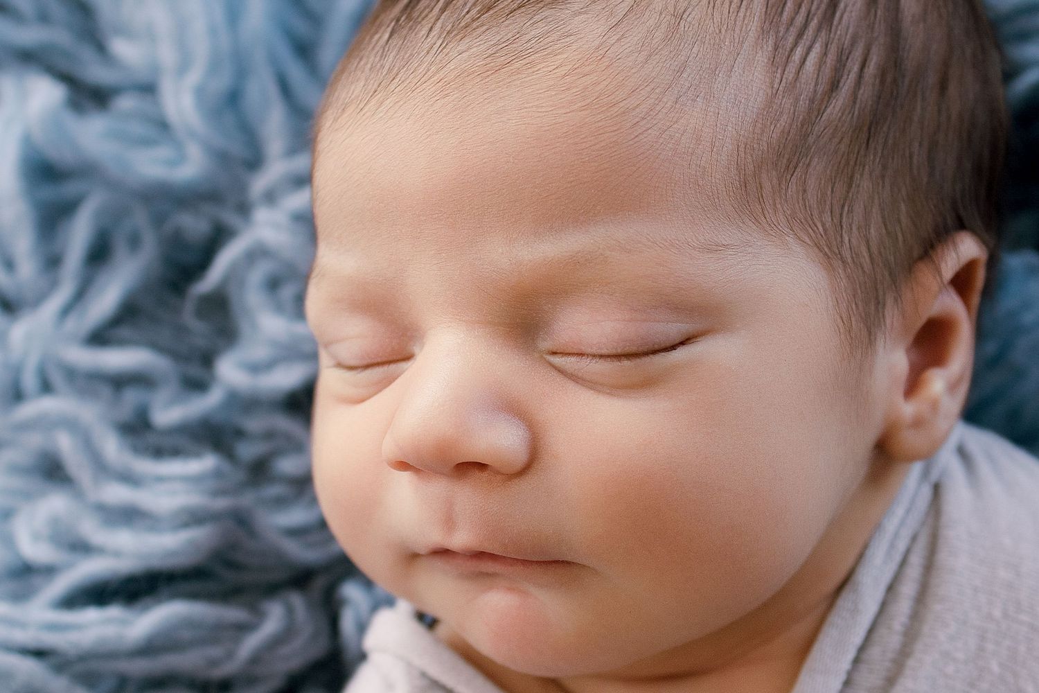 Peaceful newborn baby sleeping on a soft blue textured blanket, close-up portrait photography.