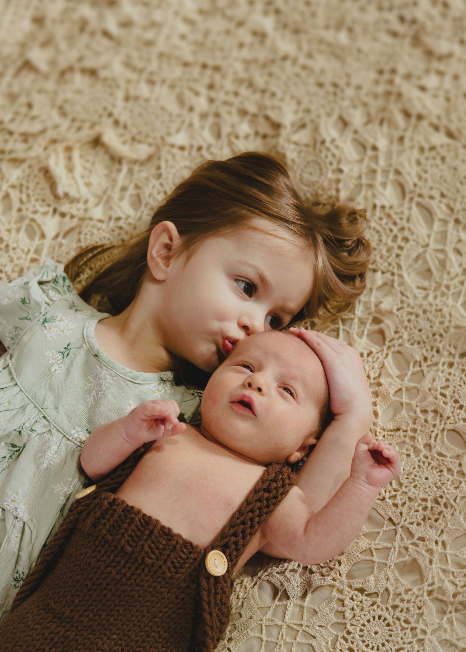 Two figures in matching light dresses resting on lace fabric.