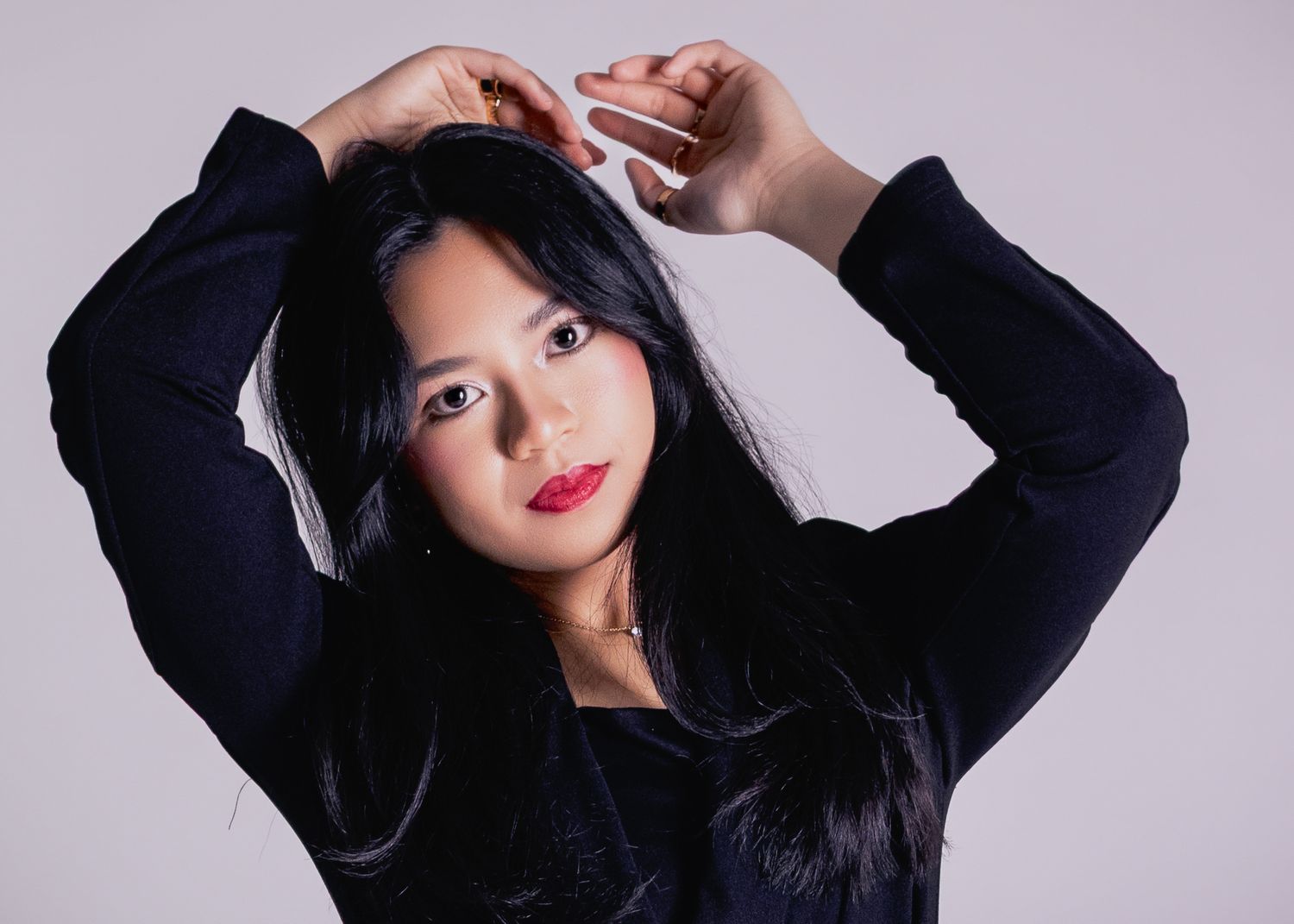 Young Asian woman with long black hair poses confidently in a dark blue top against a light gray background.