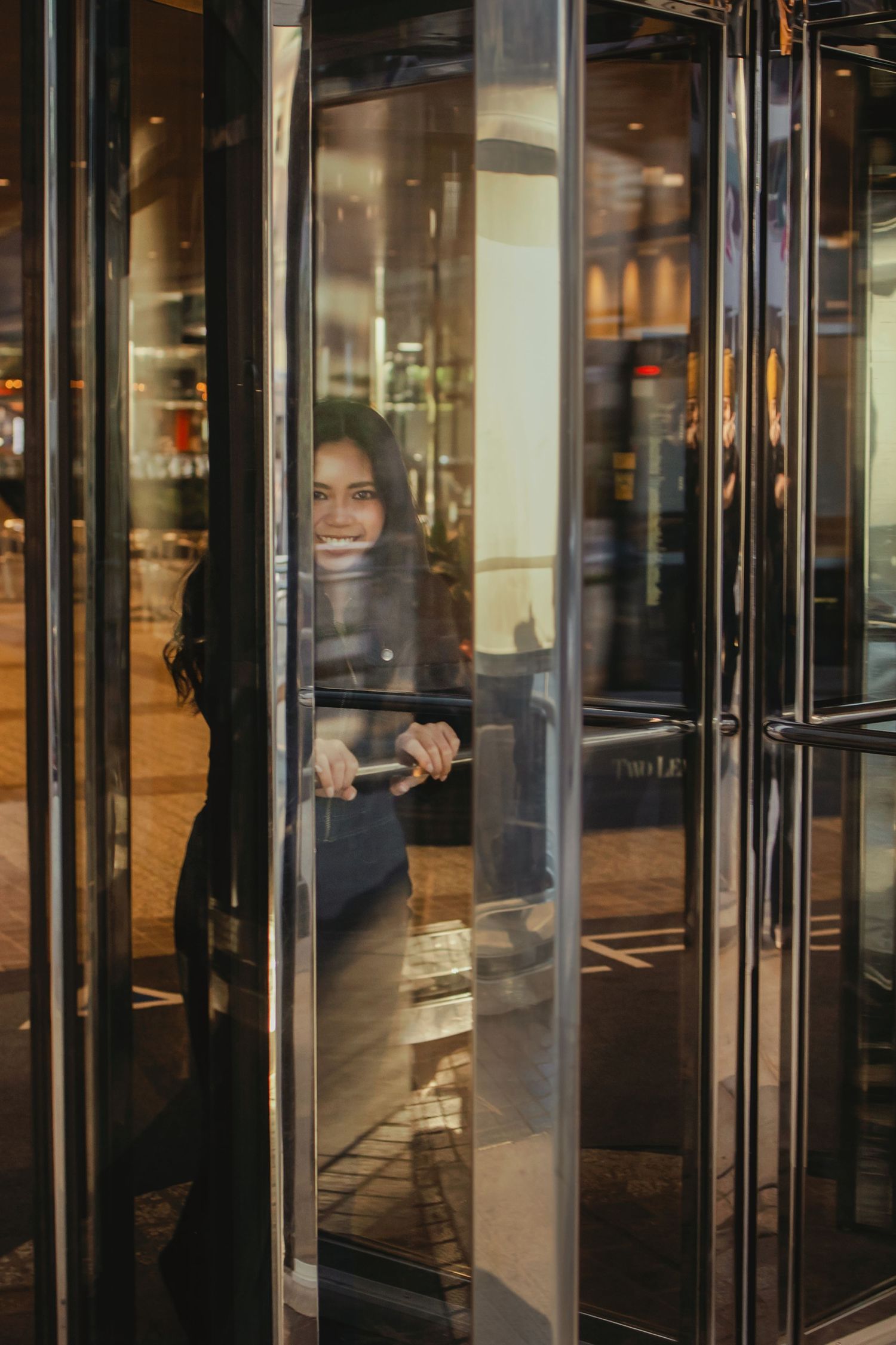 Smiling young woman pushing through revolving glass door of upscale building.