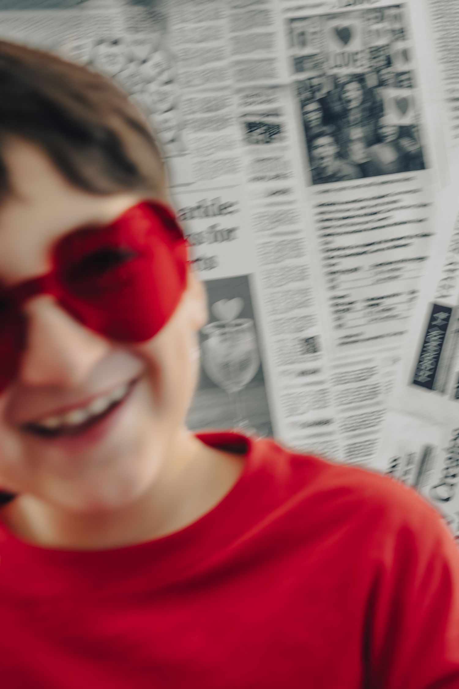 Smiling boy wearing red heart-shaped sunglasses and red shirt posed in front of newspaper background.