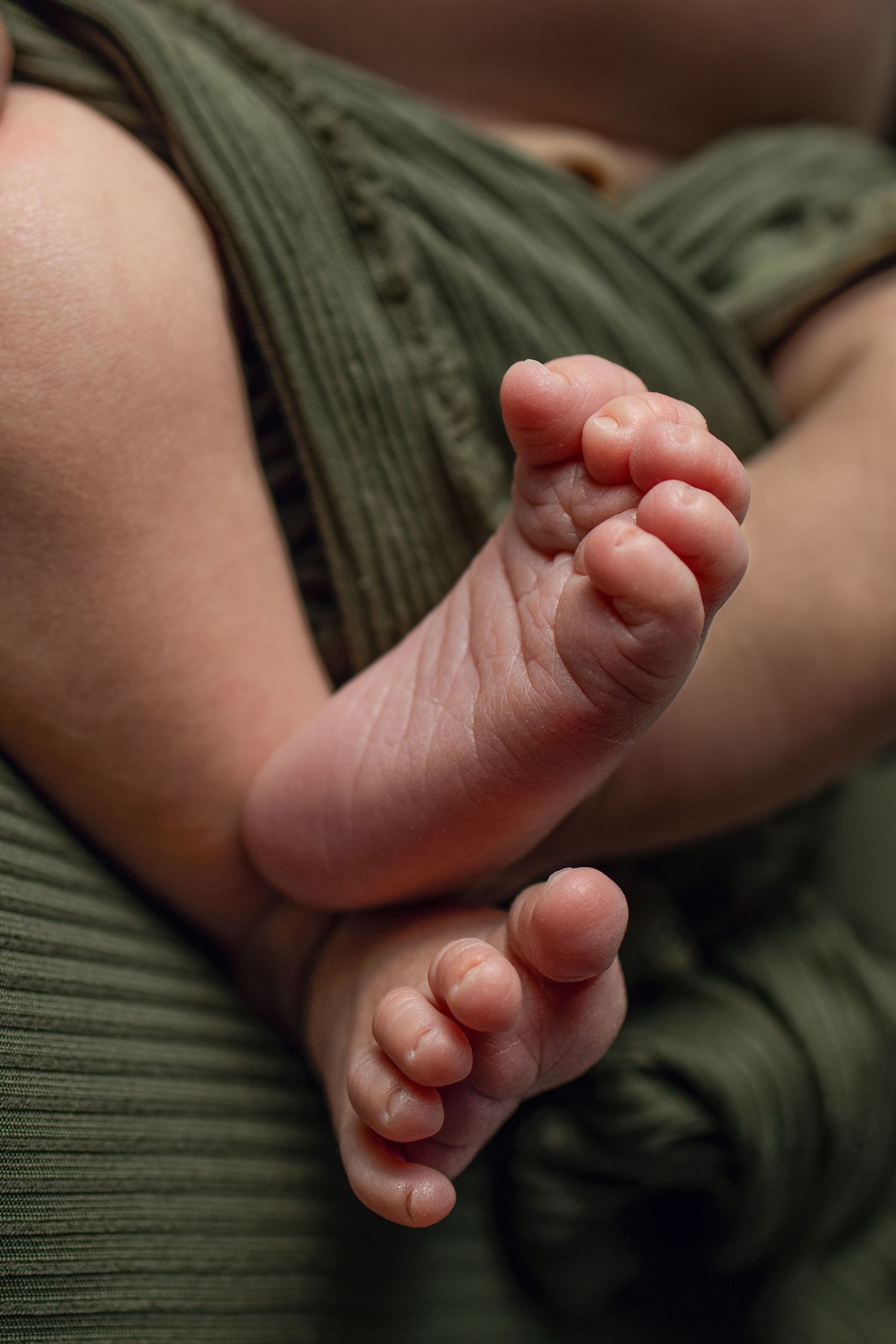 Close-up of tiny newborn baby feet wrapped in a soft green textured blanket.