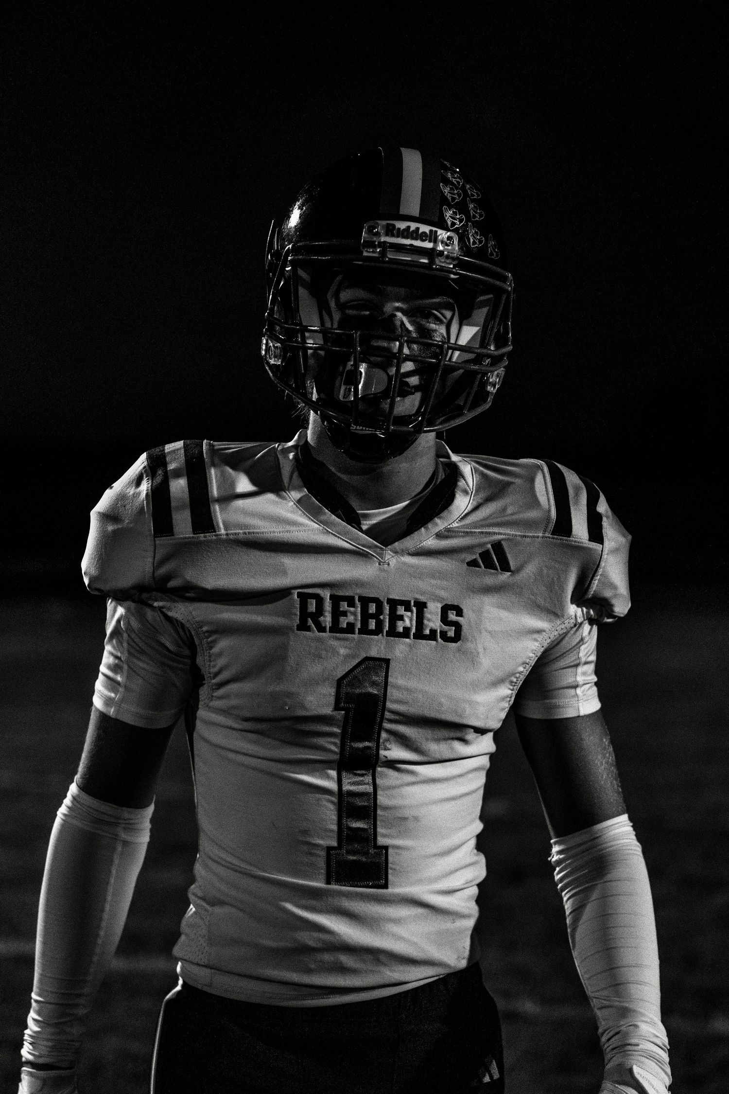 A dramatic black and white portrait of a football player wearing a Rebels jersey number 1 with protective gear.