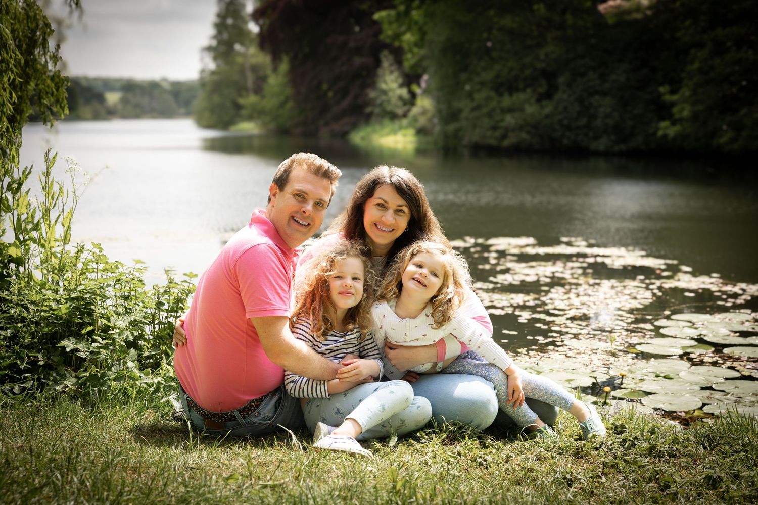 family sitting together on the grass in front of a lake
