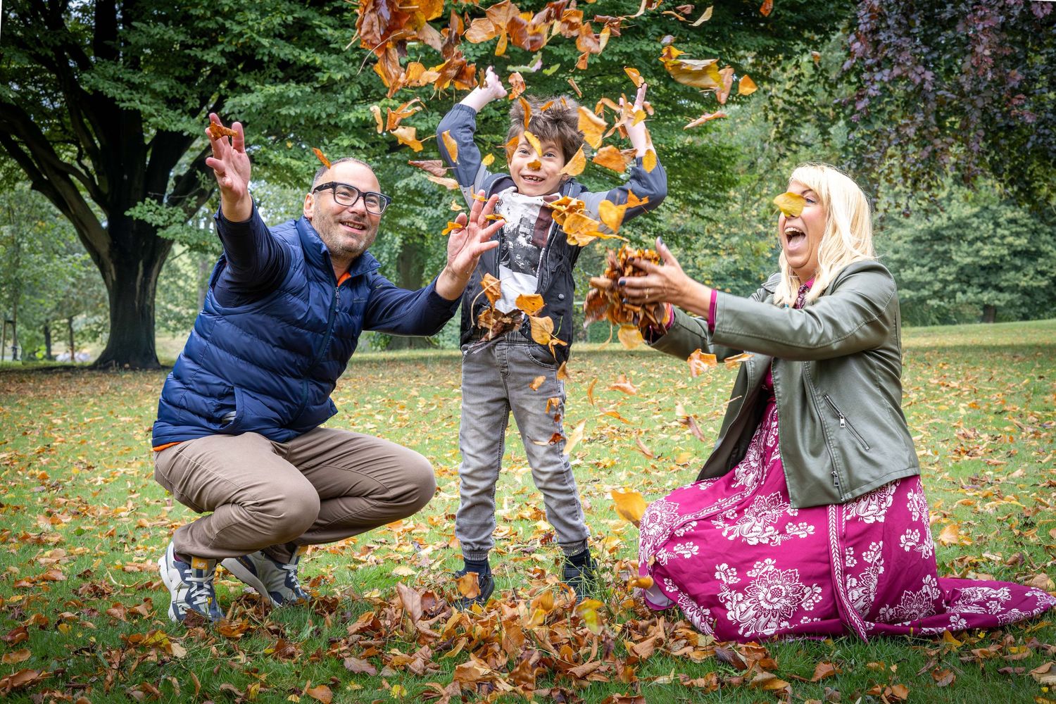 mother, child and son throwing leaves in the air in a park