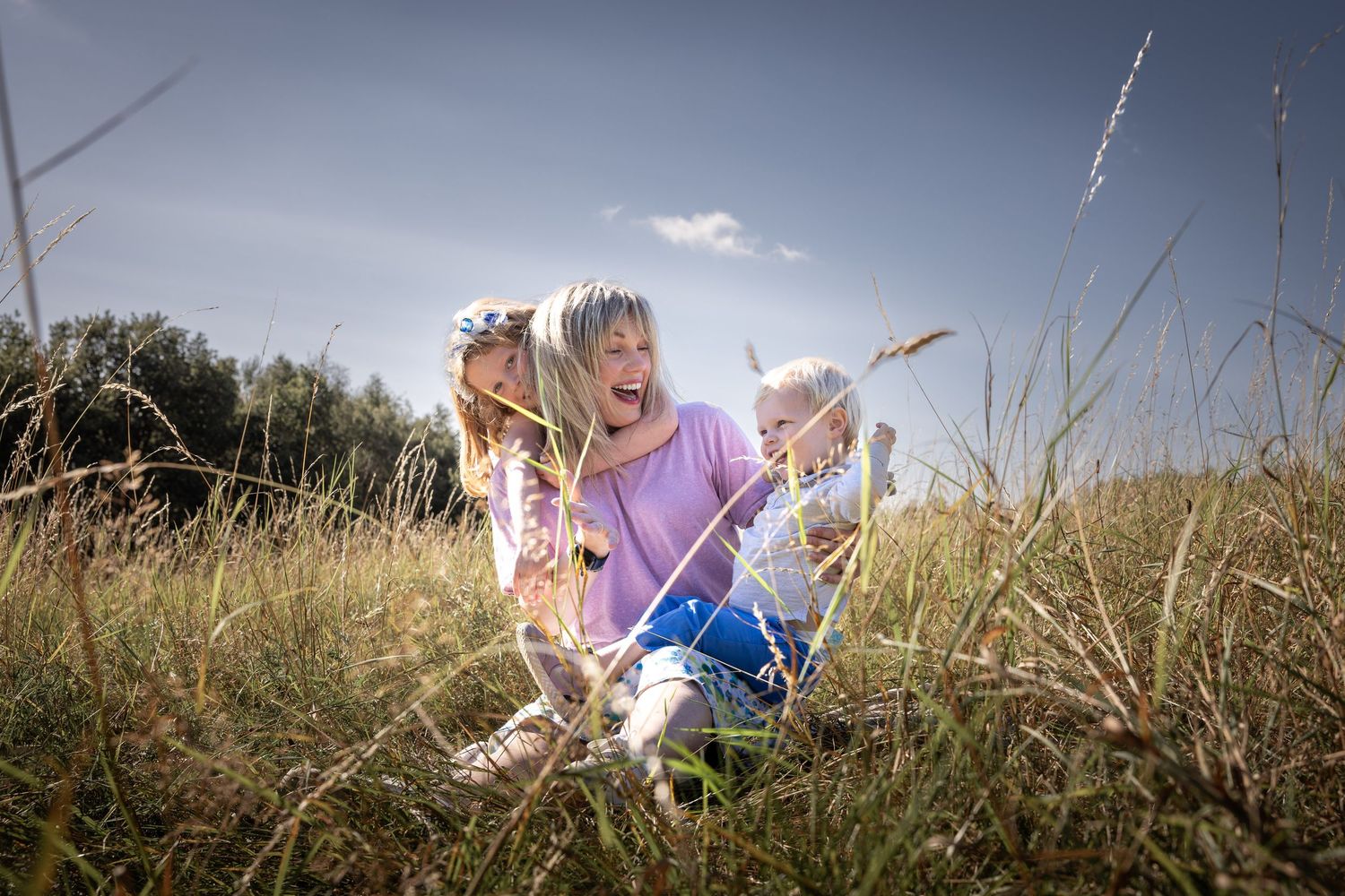 mother and children sitting in a grassy field laughing