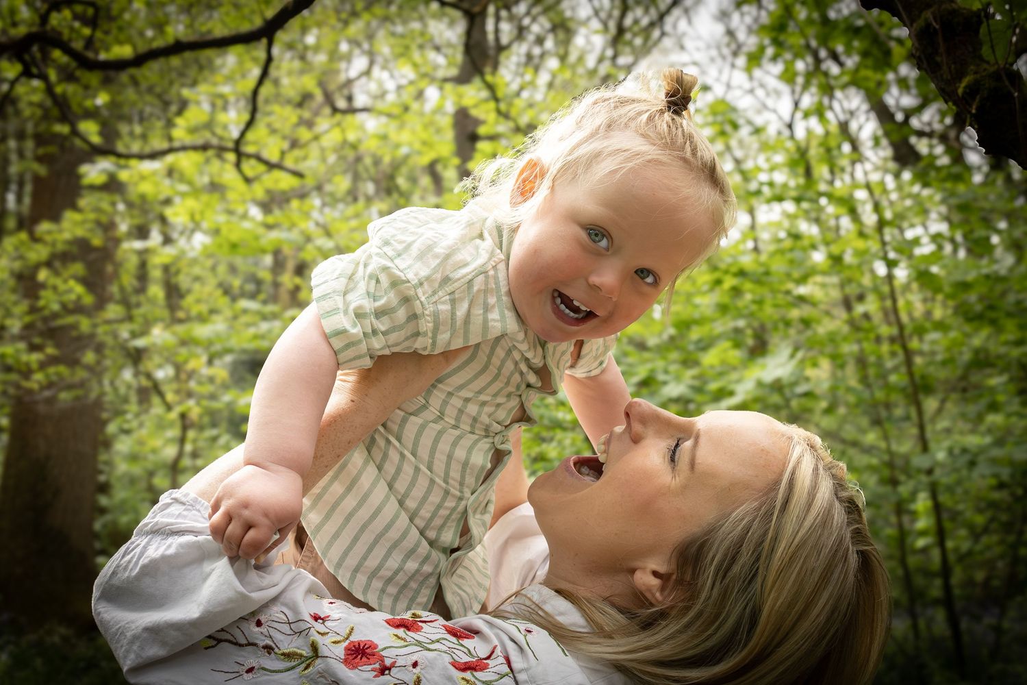 mother lifting son above her head in woodland