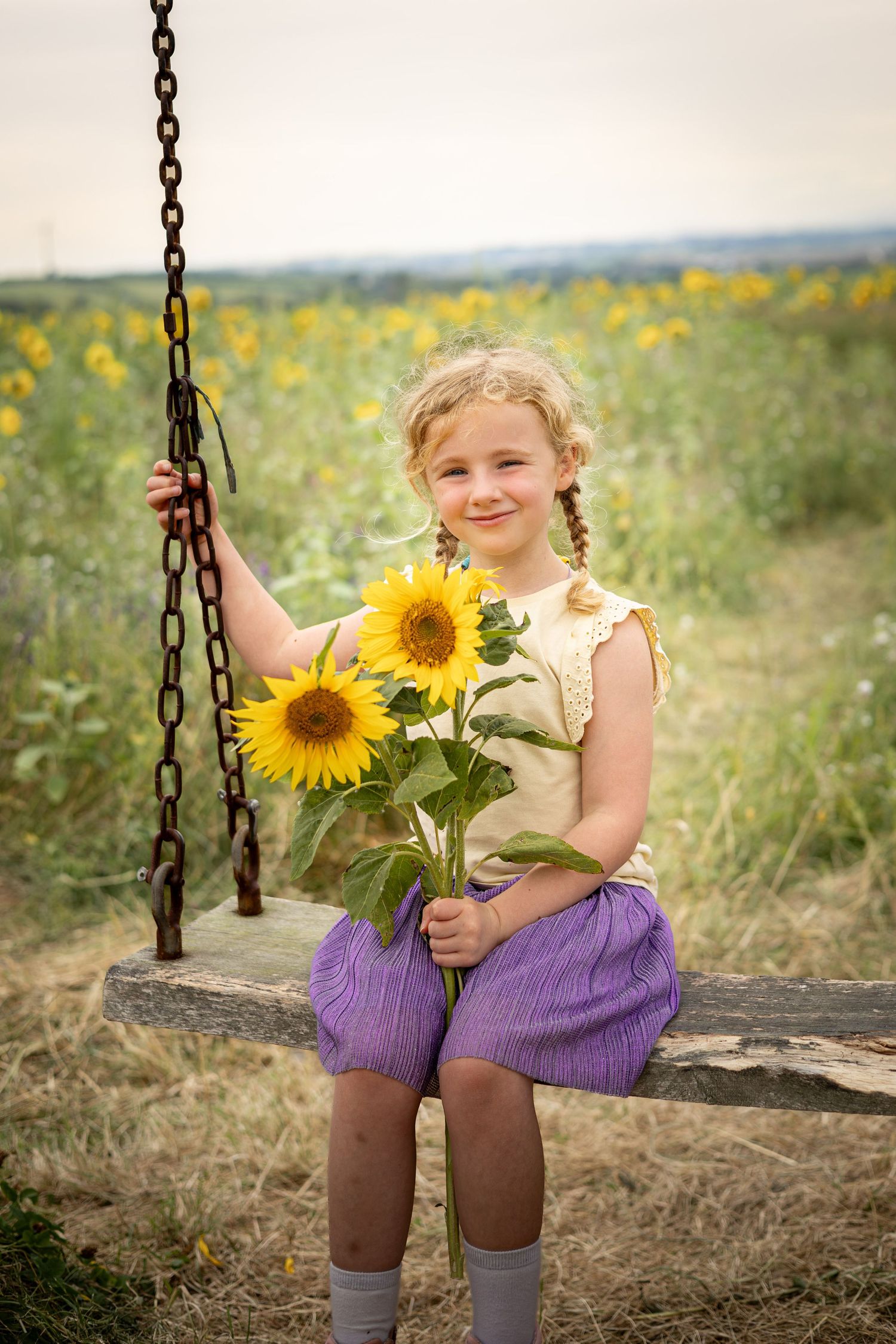 little girl sat on a swing holding sunflowers