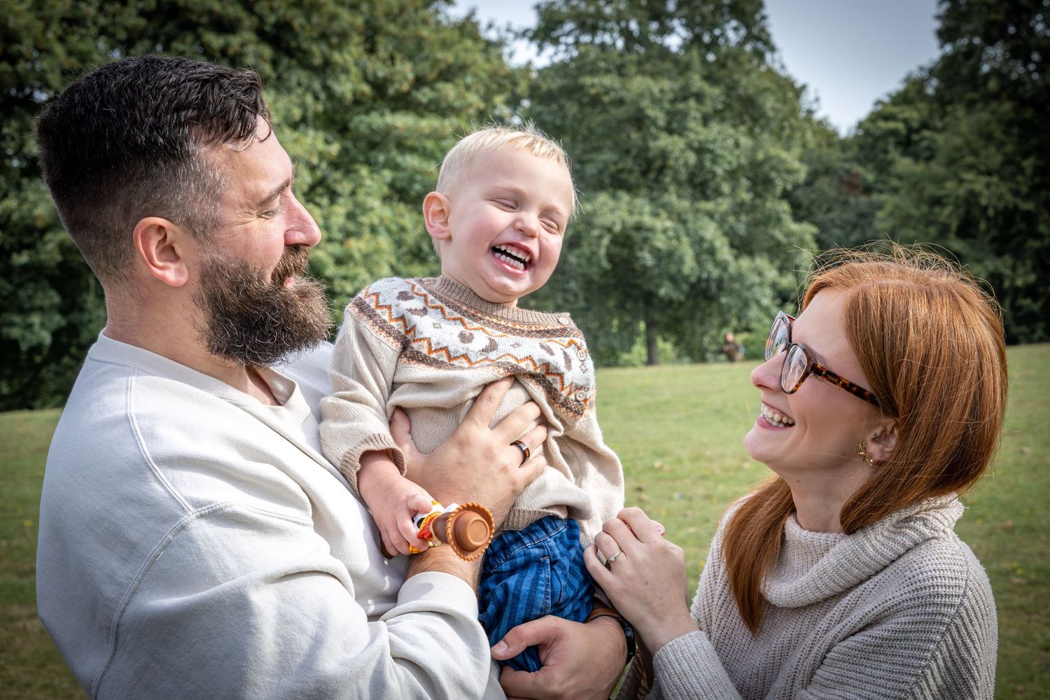 a mother and a father holding their son, laughing in a park