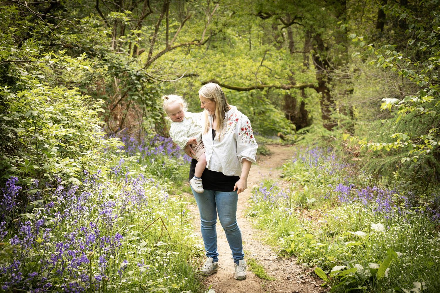 mother holding her son walking in a bluebell wood