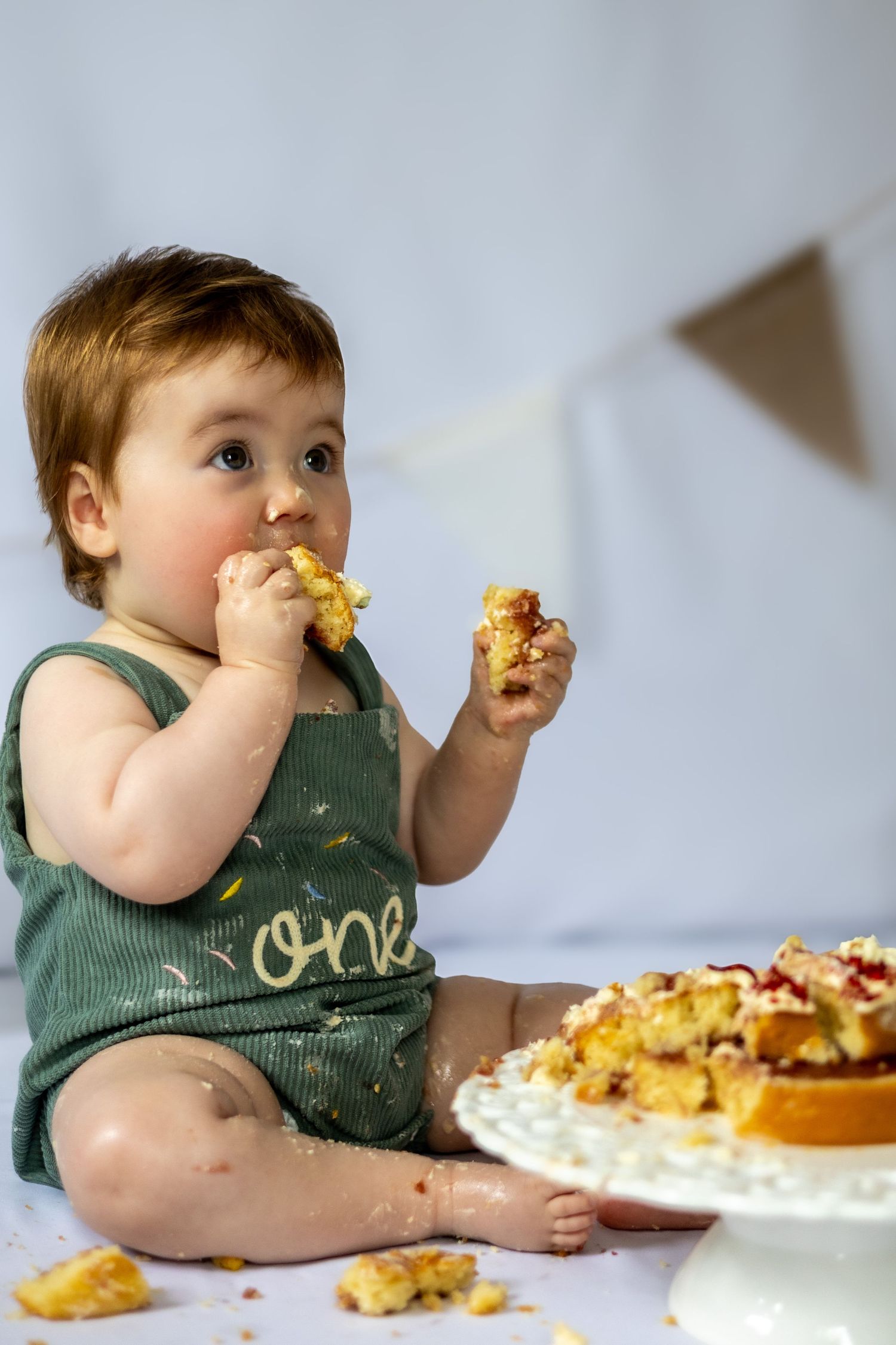 child in green dungarees eating cake