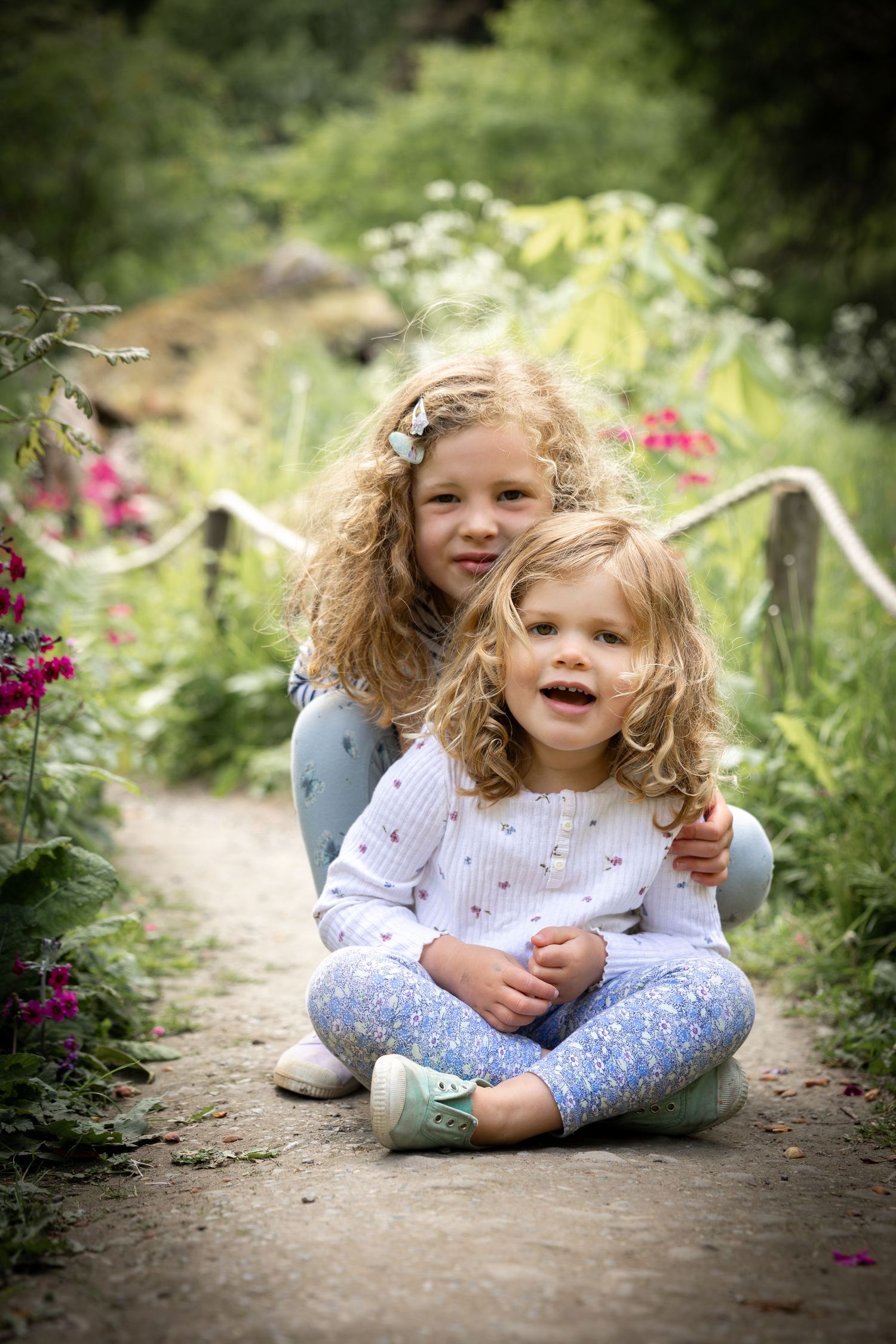 two children sitting cross legged on a path in a garden
