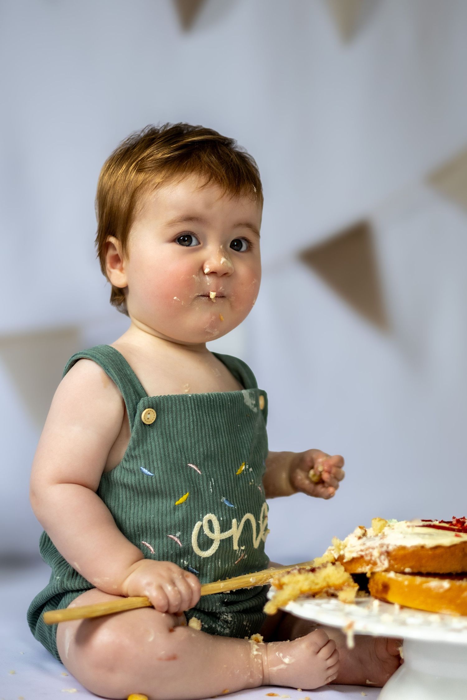 child in green dungarees eating cake