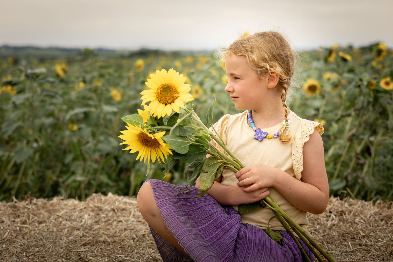 child in a yellow t-shirt holding sunflowers in a meadow