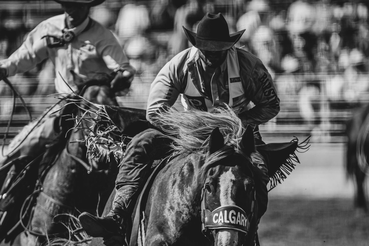 Rodeo competitors riding horses in an arena during competition.