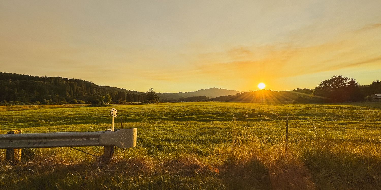 Golden sunset over rural grasslands with mountains in the distance.
