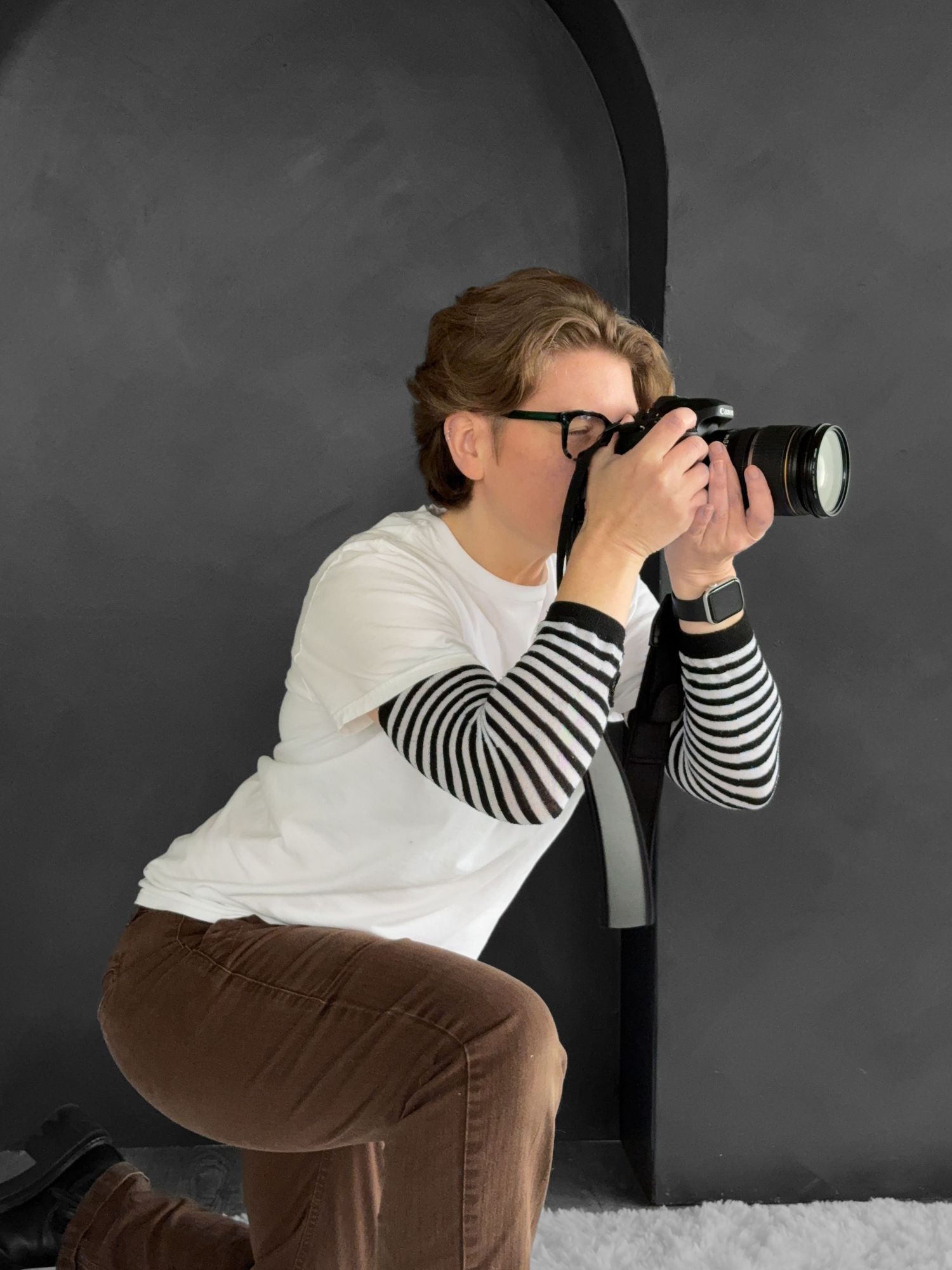 An androgynous person with short wavy hair aims a professional camera