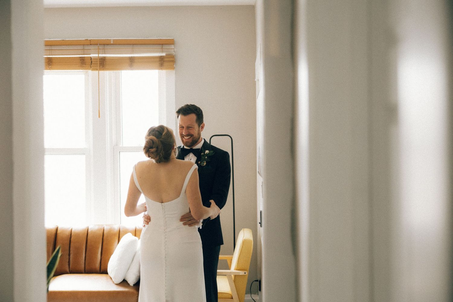 A couple shares an intimate moment in a sunlit room with bamboo shades and a brown couch.