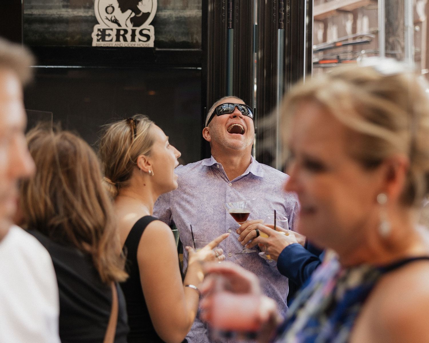 Wedding guests share laughter and drinks during an outdoor reception celebration.
