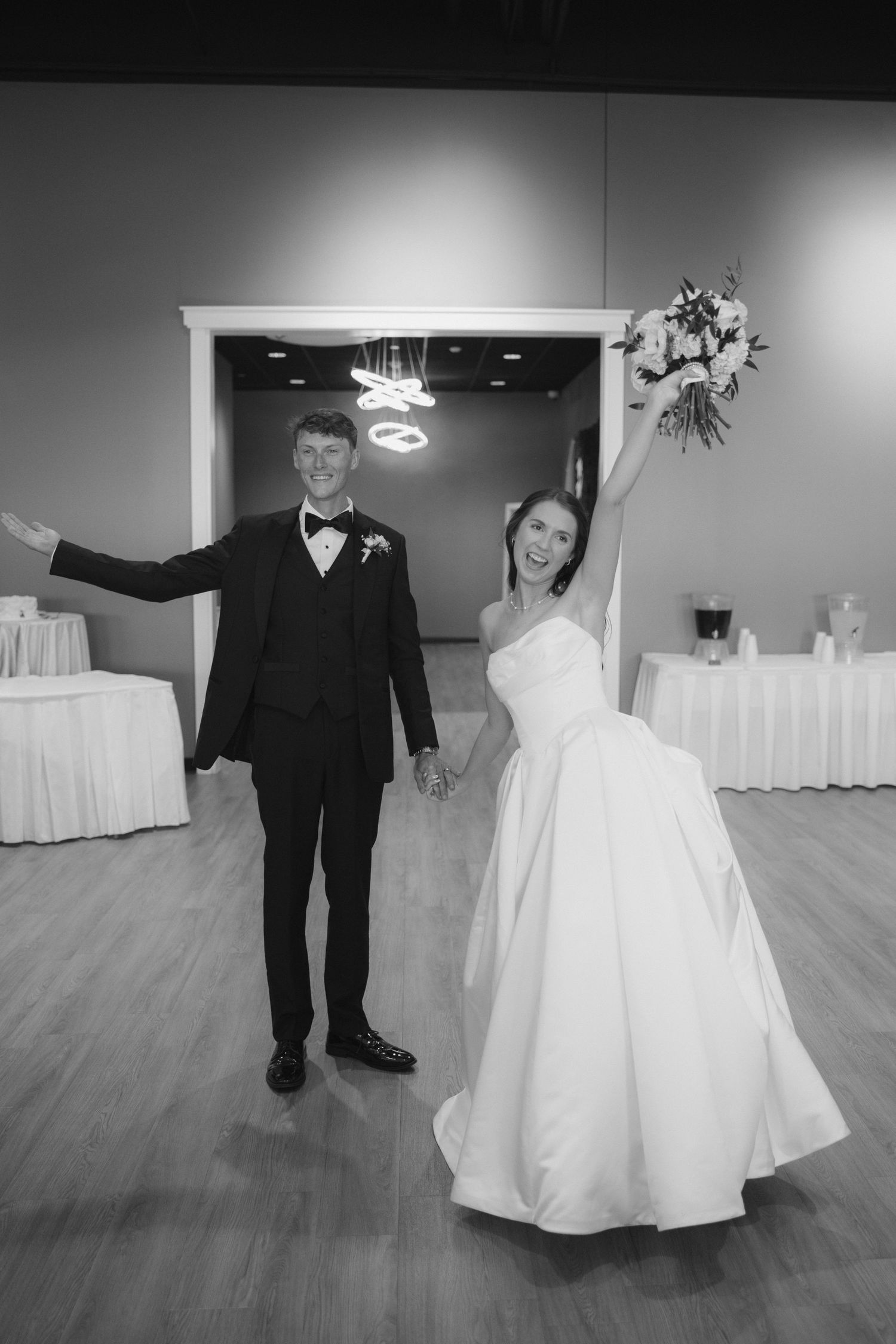 Black and white photo of a joyful bride and groom making a grand entrance at their wedding reception.