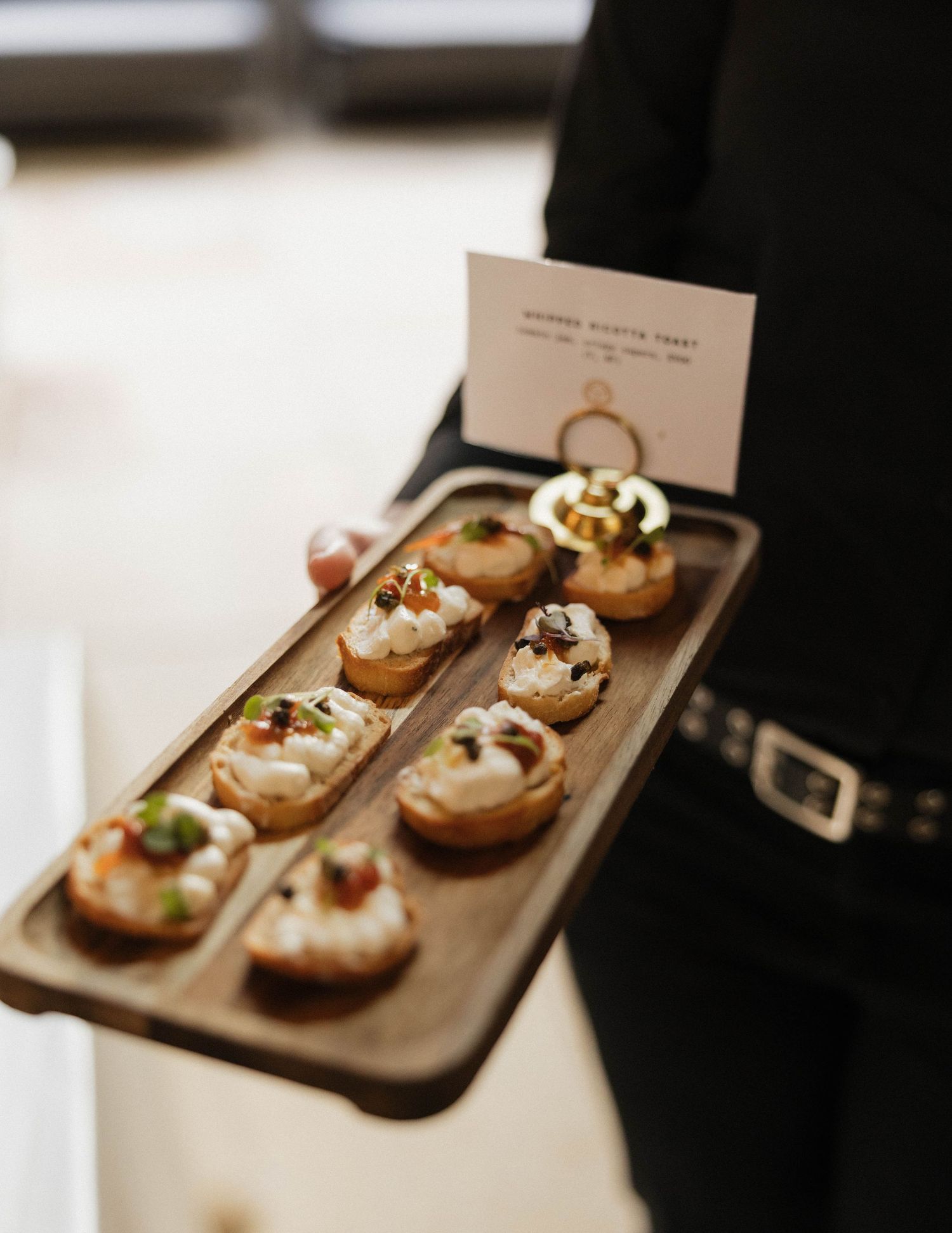 Server presenting wooden tray of gourmet bruschetta appetizers with menu card at wedding reception.