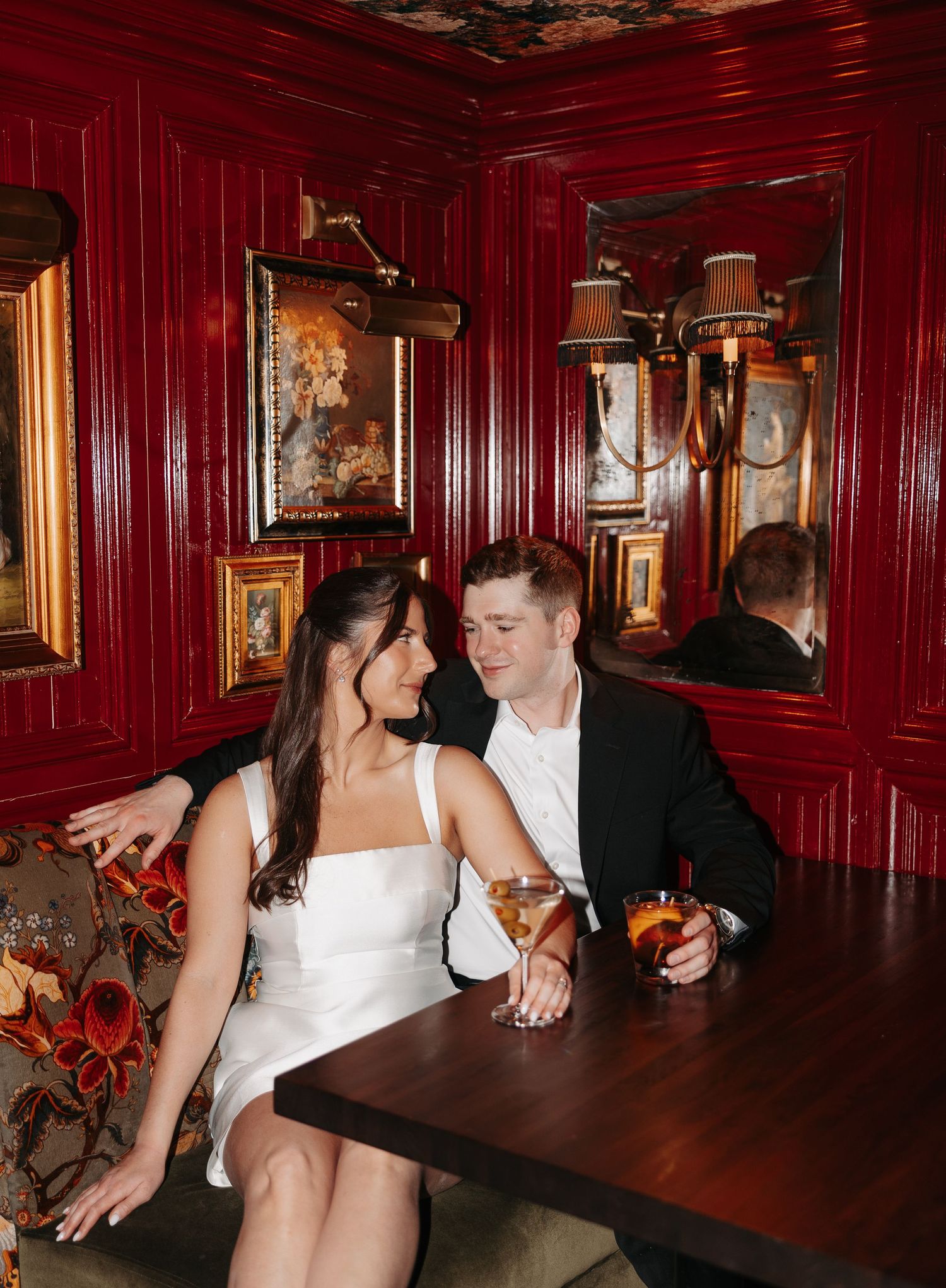 A couple shares an intimate moment at a table in a dimly lit restaurant with red walls and vintage decor.