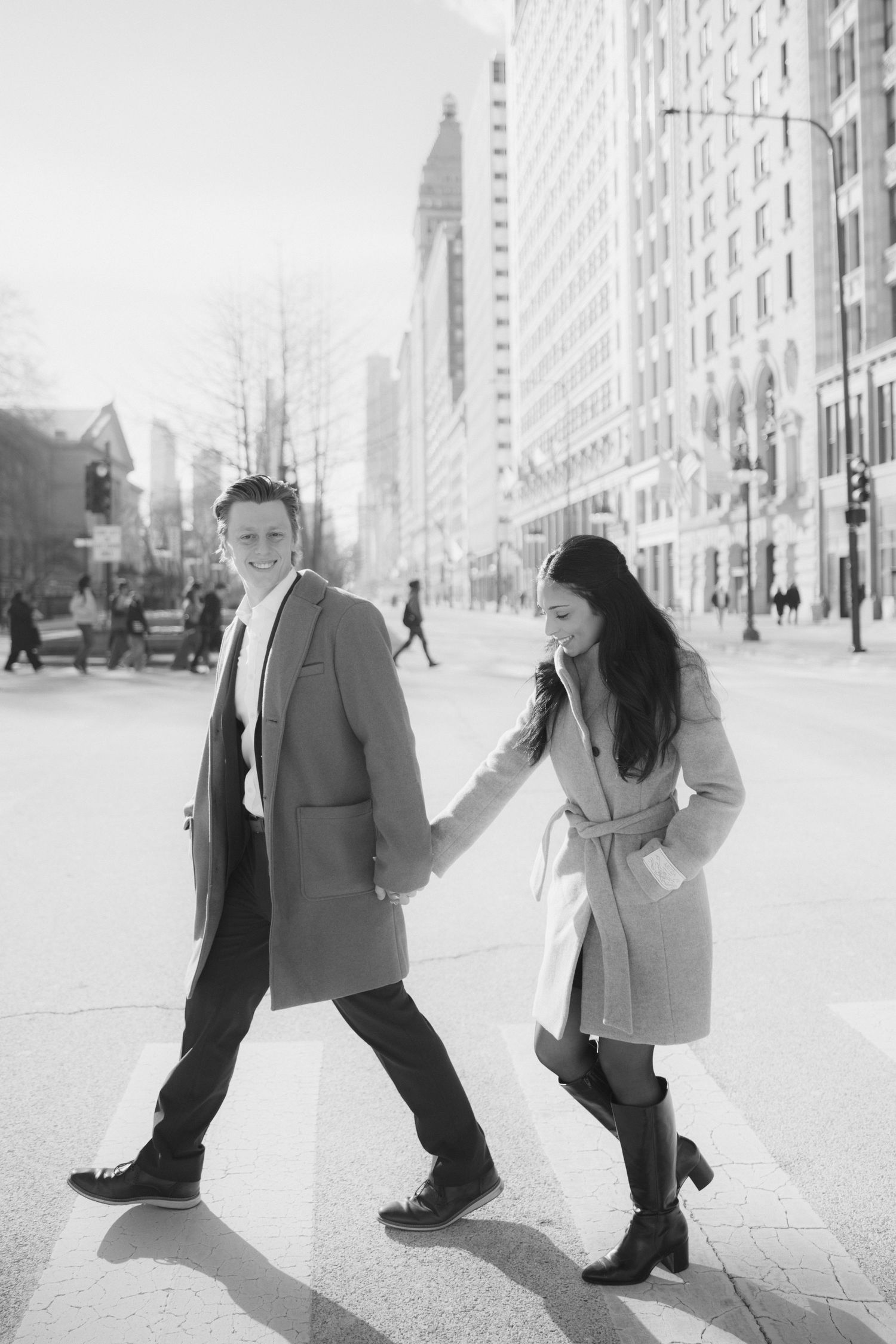 Playful couple poses on a city sidewalk with tall buildings in the background.