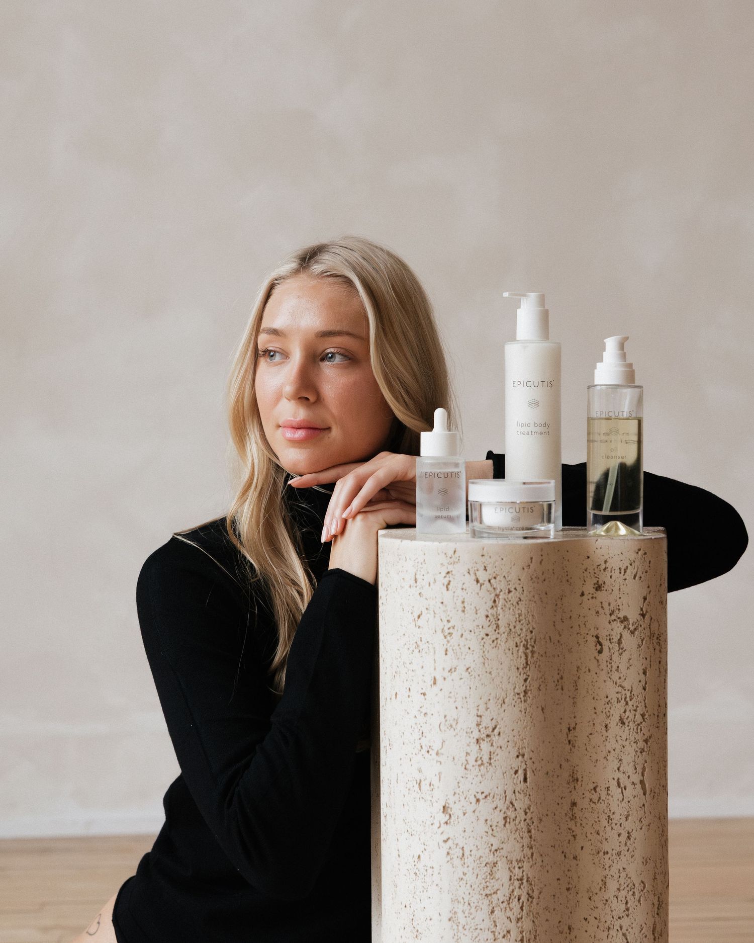 A collection of skincare products displayed on a textured concrete pedestal with a minimalist aesthetic.