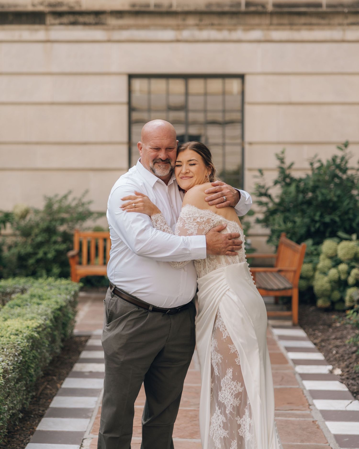A tender first look moment between a couple in formal wedding attire sharing an embrace in a garden setting.