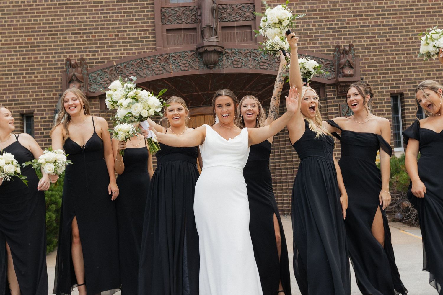 Bridesmaids in black dresses pose for group photos outside a brick building.